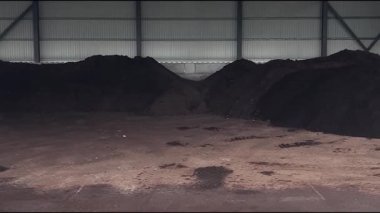 Cesis, Letonya - 21 Kasım 2025: Geniş bir depodaki karanlık toprak yığınları boyunca kameralar, endüstriyel ortamdaki materyallerin dokularını ve derinliklerini gösteriyor