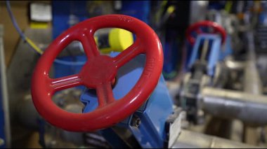 Cesis, Letonya - 21 Kasım 2025: Endüstriyel ortamda kırmızı valf tekerleğine yakın çekim, kamera karmaşık makine ve dokuları ortaya çıkarmak için yakınlaşıyor