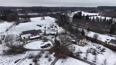 Cesis, Letonya - 21 Kasım 2025: Hava görüntüsü karlı kırsal araziyi çiftlik evleri ve dolambaçlı yollar ile görüntülüyor, kırsal manzarayı gösteren kamera tavaları
