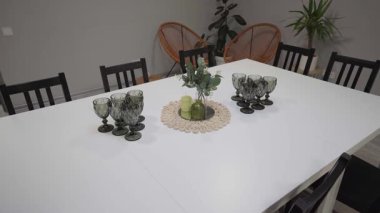 Yemek masasında dekoratif cam eşyalar ve çiçekli bir süs eşyası, modern dekor ve mekan düzenini ortaya çıkarmak için davetkar bir atmosfer, kamera tavaları ve kamera var.