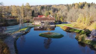 Sigulda, Letonya - 14 Ekim 2019: Güzel bir sonbahar sahnesi, içinde ev, renkli ağaçlar ve fotoğraf makineleri bulunan huzurlu bir gölü gözler önüne seriyor