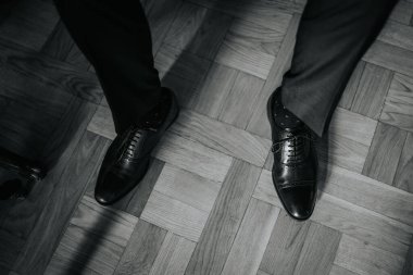 Siyah ayakkabılar ahşap döşemede zarif bir şekilde sergileniyor, sahnenin resmi kıyafetlerini ve sofistike atmosferini vurguluyor.