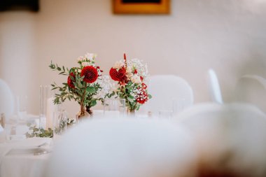 Yemek masasındaki cam vazolarda kırmızı ve beyaz çiçekli güzel çiçek süslemeleri kutlama ve toplanma ortamını güçlendiriyor.