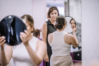 Güzellik salonundaki kadın imajını yansıtan yuvarlak bir ayna tutarken, başka bir kadın da kendi kişisel bakım ve bakım ortamını yaratıyor.