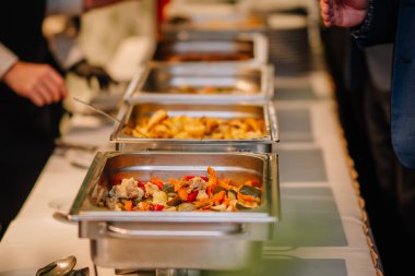 Büfe vitrininde bir dizi metal tepsi, renkli sebzeler ve etler yer alıyor, konukları enfes bir aşçılık deneyimi yaşamaya davet ediyor.