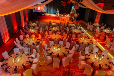 Kutlama için şölen salonu, zarif dekorlar ve yumuşak ışıklandırmayla süslenmiş yuvarlak masalar, konuklar için sıcak ve davetkar bir ortam yaratıyor.