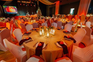 Şenlikli bir etkinlik için dekore edilen ziyafet salonunda sıcak ışıklandırmalı ve Noel ağacıyla süslenmiş masalar, kutlama atmosferini yükseltiyor.