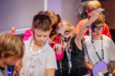 Riga, Letonya - 24 Ekim 2025 Cadılar Bayramı partisi. Yüzü boyalı çocuklar dekorasyon ve heyecanla dolu canlı bir etkinlikte eğlenceli aktivitelere katılıyorlar.