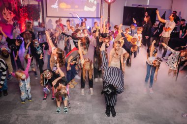 Riga, Letonya - 24 Ekim 2025 Cadılar Bayramı partisi. Cadılar Bayramı partisinde kostümlü çocuklar dans ediyor. Sis ve renkli ışıklar eğlenceli bir ortam yaratıyor.