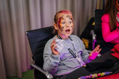 Riga, Letonya - 24 Ekim 2025 Cadılar Bayramı partisi. Renkli yüz boyalı kız, canlı dekorasyonlar ve neşeli ambiyansla çevrili festival etkinliğinde heyecan gösteriyor.