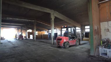 Valmiera, Letonya - 01 Ekim 2025: Asyalı erkek forklift operatörü, endüstriyel faaliyet ve iş akışı gösteren büyük bir depoda ahşap paletler taşıyor