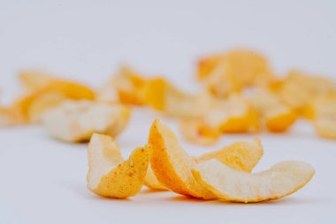 Turuncu tonlarda canlı dondurulmuş meyve dilimleri temiz beyaz bir arka plana sanatsal olarak dağılmış, eşsiz dokularını ve renklerini vurguluyor, sağlıklı atıştırmalıklar için ideal.