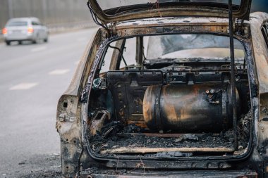Yanmış bir aracın yanmış kalıntıları, yol kenarında terk edilmiş, hasar görmüş iç organları ve bileşenleri, kentsel bozulmayı ve yangın olaylarının etkisini gösteriyor.