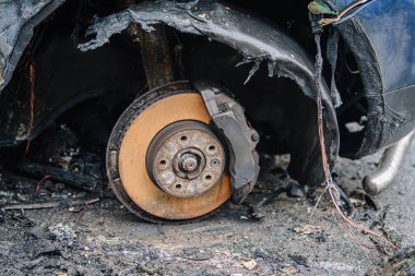 Yanmış lastik ve fren parçalarından oluşan hasarlı bir araba tekerleğinin yakın çekimi, görünür mekanik detaylar ve dokularla meydana gelen bir kazanın sonucunu gösteriyor