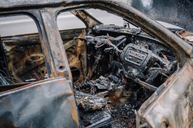 Yanmış bir arabanın içinde ağır yangın hasarı, yanmış malzemeler ve erimiş bileşenler görülüyor. Araç yangınının yıkıcı etkilerini vurguluyor.