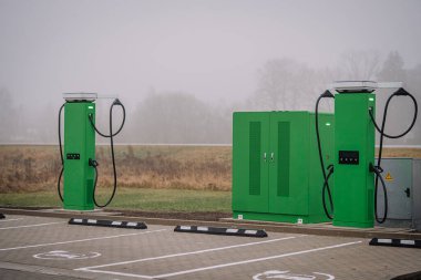 Elektrikli araç şarj istasyonları, sürdürülebilir enerji ve modern ulaşım çözümlerinin önemini vurgulayan sisli bir ortamda konumlandırılmış, parlak yeşil tasarım içerir