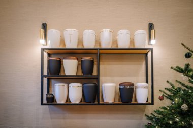 Modern seramik vazolar dekoratif bir rafta dizilmiş, çeşitli renk ve desenlere sahip, duvar aplikleriyle aydınlatılmış, sıcak ve davetkar bir atmosfer yaratıyor.