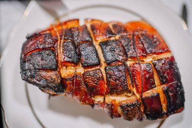 Dilimlenmiş kızarmış domuz göbeği, altın çıtırdıyor, beyaz bir tabakta zarif bir şekilde düzenleniyor, leziz dokuları vurguluyor ve yemek sevenler için davetkar bir sunum yapıyor.