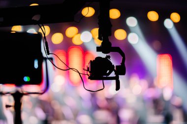 Titreşimli bir dengeleyiciye sahip kamera teçhizatı, canlı bir sahne arkaplanına karşı ayarlanır, parlak ışıklar ve bulanık renkler sergilenir, bir performansın atmosferini yükseltir