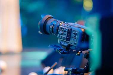 Tripod üzerindeki video kamera, renkli ışıklandırma ve bulanık çevreyle dinamik olay sahnesini yakalıyor, modern çekim ekipmanlarını ve yaratıcı potansiyeli vurguluyor.