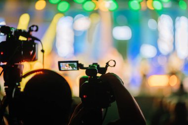 İki kamera operatörü parlak sahne ışıkları ve bulanık bir izleyiciyle canlı bir konser çekiyorlar. İzleyiciler için enerjik ve dalgın bir atmosfer yaratıyorlar.