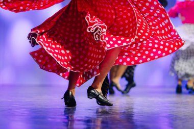 Canlı Letonyalı halk dansçıları, kültürel miraslarını ve geleneksel dans hareketlerini vurgulayan renkli kostümler giyerek sahnede enerjik bir performans sergiliyorlar.