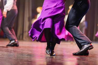 Renkli kostümlü dansçılar, kültürel ifade ve dinamik ayak hareketlerini vurgulayarak sahnede geleneksel Letonya halk dansı yapıyorlar.