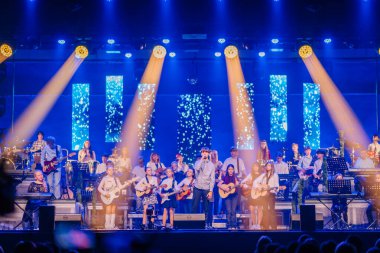 Valmiera, Letonya - 29 Aralık 2025: Yamaha. Bir grup genç müzisyen renkli ışıklar ve enstrümanlarla sahnede performans sergiliyor ve enerjik bir atmosfer yaratıyorlar.