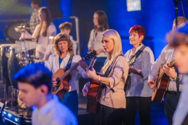 Valmiera, Letonya - 29 Aralık 2025: Yamaha. Sahnede canlı mavi ışıklandırmayla gitar ve perküsyon enstrümanları çalan bir grup bayan müzisyen