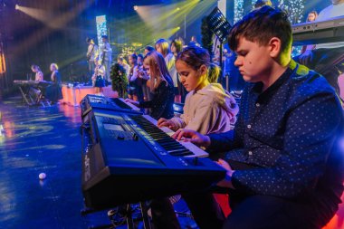 Valmiera, Letonya - 29 Aralık 2025: Yamaha. Çocuklar canlı bir konser sırasında sahnede klavye çalıyorlar. Parlak ışıklar ve şenlikli dekorasyonlar atmosferi geliştiriyor.