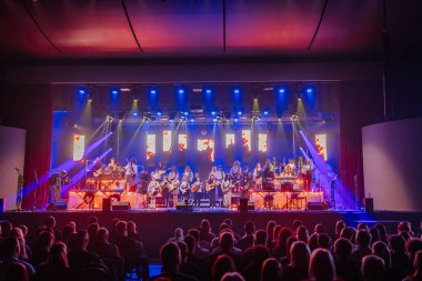 Valmiera, Letonya - 29 Aralık 2025: Yamaha. Çeşitli müzisyen grupları renkli ışıklarla sahnede canlı performans sergiliyor ve bir konser salonunda seyirci buluyor.