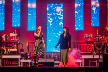 Valmiera, Letonya - 29 Aralık 2025: Yamaha. Kadın vokalistler sahnede dinamik ışıklandırma ve arka planda renkli görsellerle seyircileri cezbediyor.