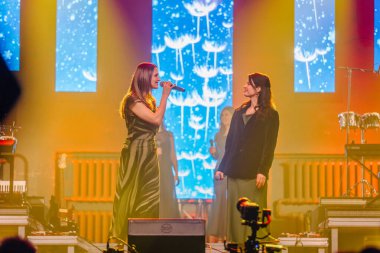 Valmiera, Letonya - 29 Aralık 2025: Yamaha. Kadın vokalistler canlı performans sırasında renkli bir ışıklandırma ve canlı bir fon ile sahnede şarkı söylüyorlar.