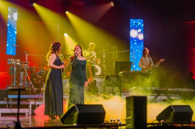 Valmiera, Letonya - 29 Aralık 2025: Yamaha. Kadın vokalistler, renkli ışıklarla ve arkalarında canlı müzik grubuyla seyircileri büyülüyor.