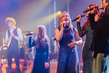 Valmiera, Letonya - 29 Aralık 2025: Yamaha. Sahnede canlı performans sergileyen bir grup kadın vokalist ve renkli ışıklar ve enerjik bir atmosfer yaratan bir grup.