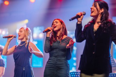 Valmiera, Letonya - 29 Aralık 2025: Yamaha. Kadın vokalistler sahnede tutkuyla şarkı söylüyorlar, renkli ışıklarla aydınlatılarak, canlı bir performans ortamı yaratıyorlar.