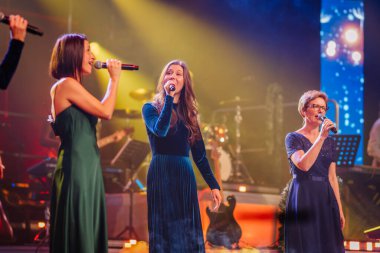 Valmiera, Letonya - 29 Aralık 2025: Yamaha. Sahnede canlı ışıklar ve müzik aletleriyle çevrili kadınlar, enerjik bir atmosfer yaratıyor.