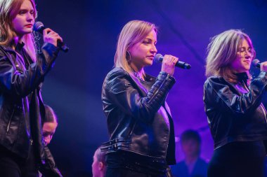 Valmiera, Letonya - 29 Aralık 2025: Yamaha. Kadın vokalistler, renkli ışıklar ve enerjik bir kalabalıkla çevrili bir şekilde sahnede tutkuyla şarkı söylüyorlar.