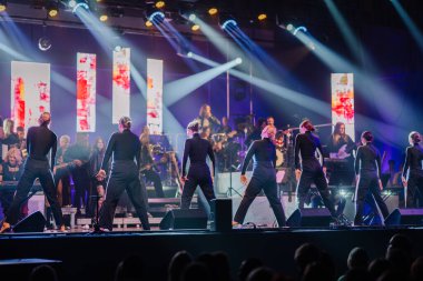 Valmiera, Letonya - 29 Aralık 2025: Yamaha. Siyah elbiseli dansçılar canlı ışıklar ve enerjik bir atmosfer yaratan müzisyenlerle sahnede gösteri yapıyorlar.