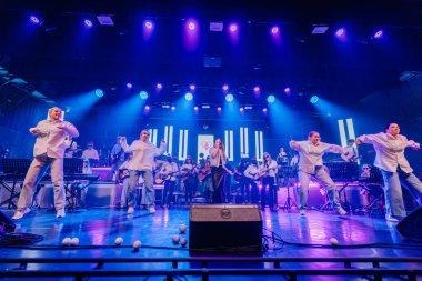 Valmiera, Letonya - 29 Aralık 2025: Yamaha. Dinamik sahne performansında müzisyenler ve dansçılar renkli ışıklarla aydınlatılarak çekici bir atmosfer yaratıyorlar.