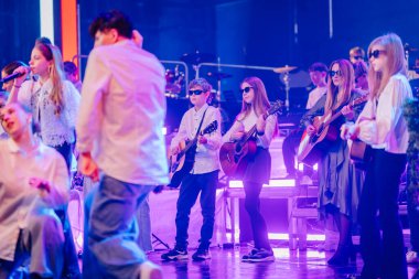 Valmiera, Letonya - 29 Aralık 2025: Yamaha. Genç müzisyenler sahnede gitar çalıyor, güneş gözlüğü takıyor ve canlı bir konser ortamı yaratıyorlar.