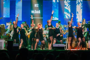 Valmiera, Letonya - 29 Aralık 2025: Yamaha. Kadın dansçılar sahnede enerjik bir performans sergiliyorlar. Arka planda renkli ışıklar ve müzisyenler var.