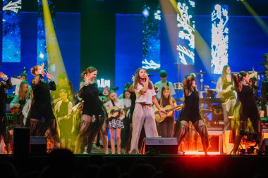 Valmiera, Letonya - 29 Aralık 2025: Yamaha. Sahnede renkli ışıklar ve arka planda enstrüman çalan müzisyenlerle şarkı söyleyen bir grup kadın sanatçı