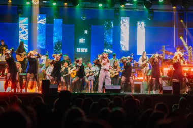 Valmiera, Letonya - 29 Aralık 2025: Yamaha. Sahneyi aydınlatan parlak ışıklarla renkli kostümlü müzisyenler ve dansçıların dinamik sahne performansı