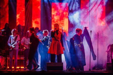 Valmiera, Letonya - 29 Aralık 2025: Yamaha. Kadın vokalist, sahne arkasında renkli ışıklar ve müzisyenlerle seyircileri cezbediyor.