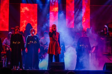 Valmiera, Letonya - 29 Aralık 2025: Yamaha. Sahnede canlı performans sergileyen bir grup kadın şarkıcı canlı ışık ve renkli dumanla enerjik bir atmosfer yaratıyor.