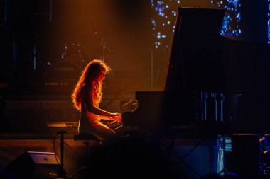 Valmiera, Letonya - 29 Aralık 2025: Yamaha. Sahnede piyano çalan kadın büyüleyici ışık efektleriyle enerjik bir konser ortamı yaratıyor.