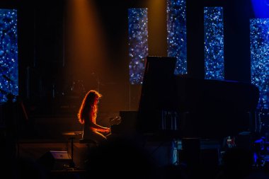 Valmiera, Letonya - 29 Aralık 2025: Yamaha. Sahnede piyano çalan kadın canlı ışıklar ve renkli ekranlarla aydınlatılarak enerjik bir atmosfer yaratıyor.