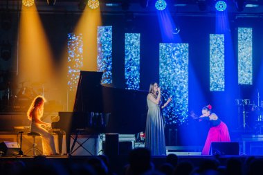 Valmiera, Letonya - 29 Aralık 2025: Yamaha. Şarkıcı, renkli ışıklar ve canlı bir konser atmosferiyle çevrili piyanist çalarken sahnede seyirciyi cezbediyor.