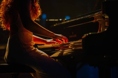 Valmiera, Letonya - 29 Aralık 2025: Yamaha. Kıvırcık saçlı kadın sahnede piyano çalıyor ve çarpıcı bir ışık büyüleyici bir atmosfer yaratıyor.